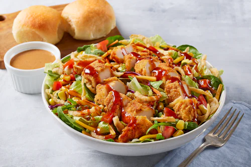 Bob Evans Wildfire Chicken Salad sitting on a table next to a small bowl of Wildfire ranch dressing and and two dinner rolls.